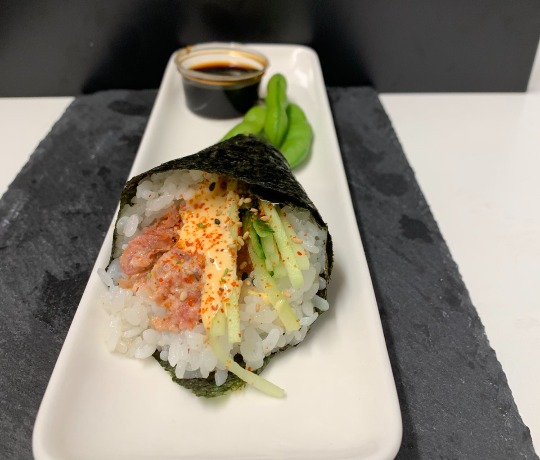 sushi on a white plate with a small pot of soy sauce, garnished with edamame